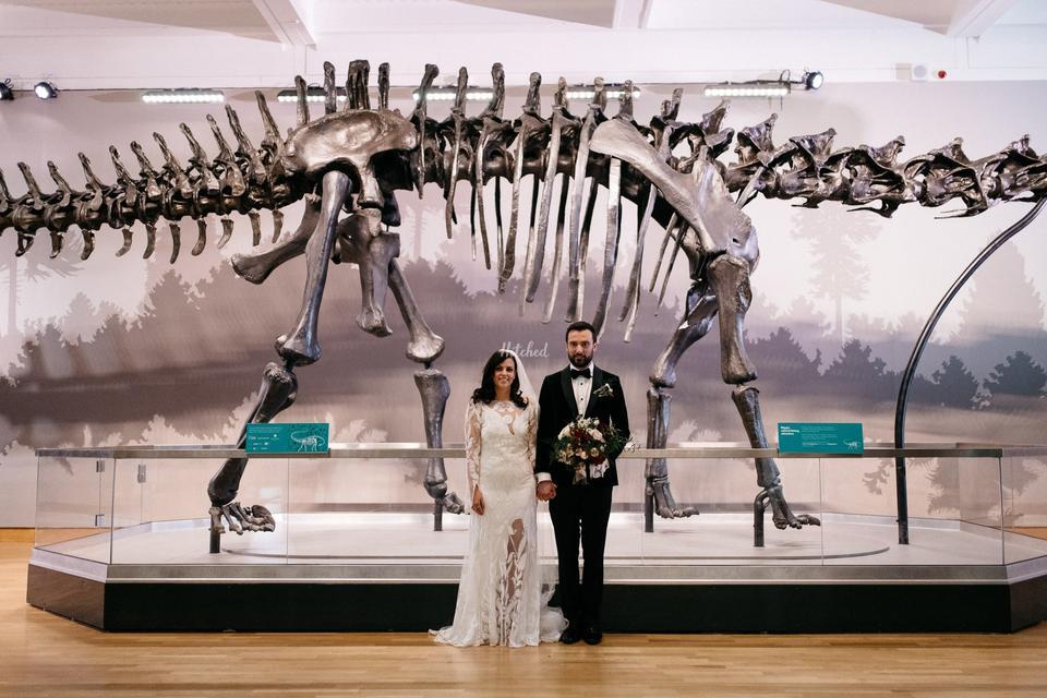 A couple poses in front of a dinosaur skeleton