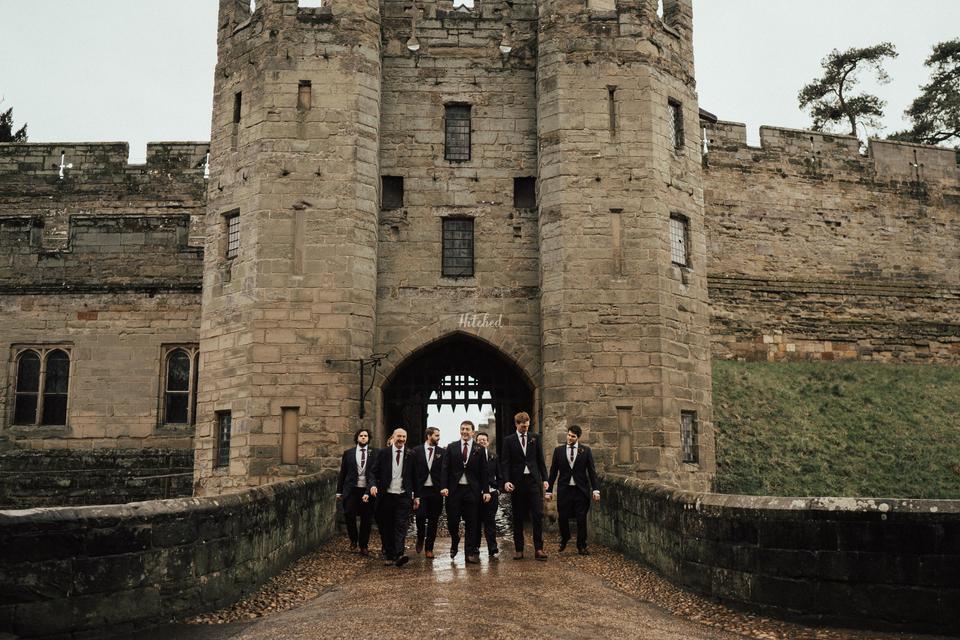 A group of groomsmen and the groom walking through the walkway at Warwick Castle