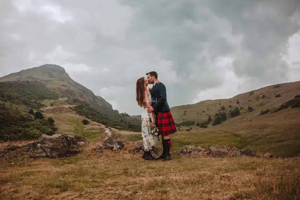 Bride and groom wearing a Scottish kilt kissing in a scenic part of the countryside in Scotland