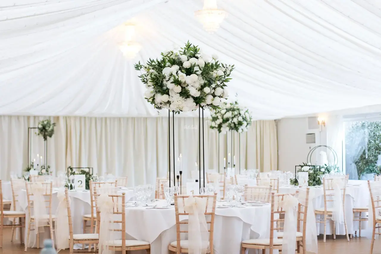 Wedding reception tables laid with white table cloths, candles and tall white floral arrangements