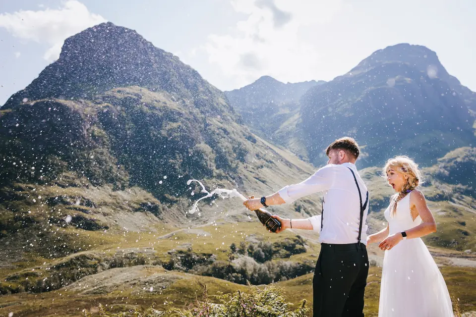 Couple looking surprised as they pop open a bottle of champagne to celebrate their wedding in the countryside of Scotland