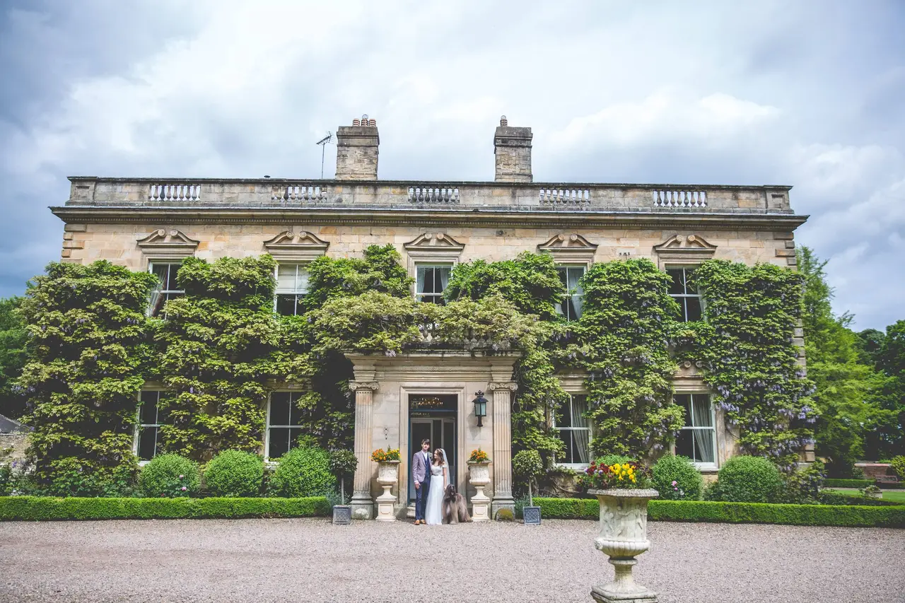 Exterior shot of Eshott Hall, a 17th Century country house, with a bride and groom standing in the doorway