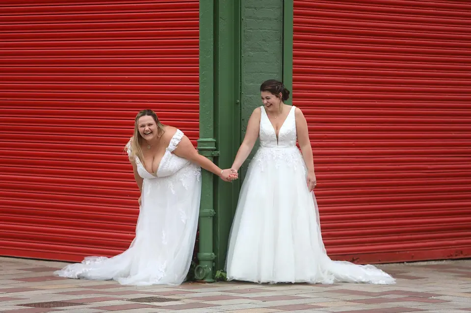 Two brides standing at a corner, one on each side, holding hands and laughing