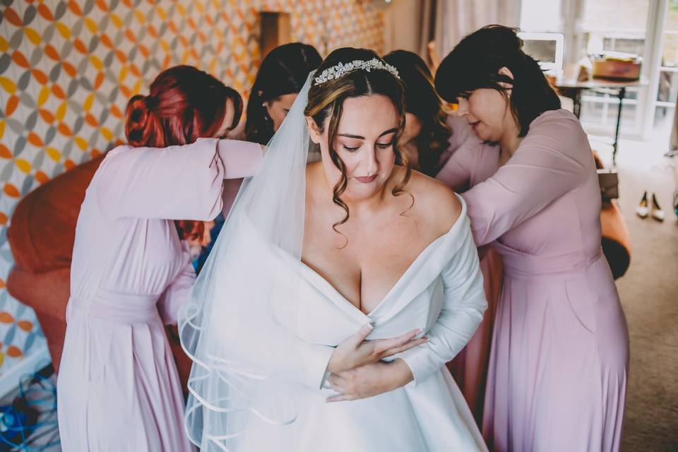 Bridesmaids fasten bride's dre