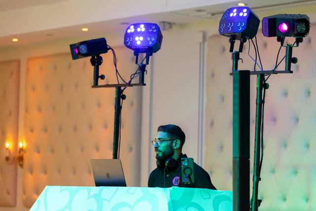 dj adjusting music on laptop under colorful spotlights