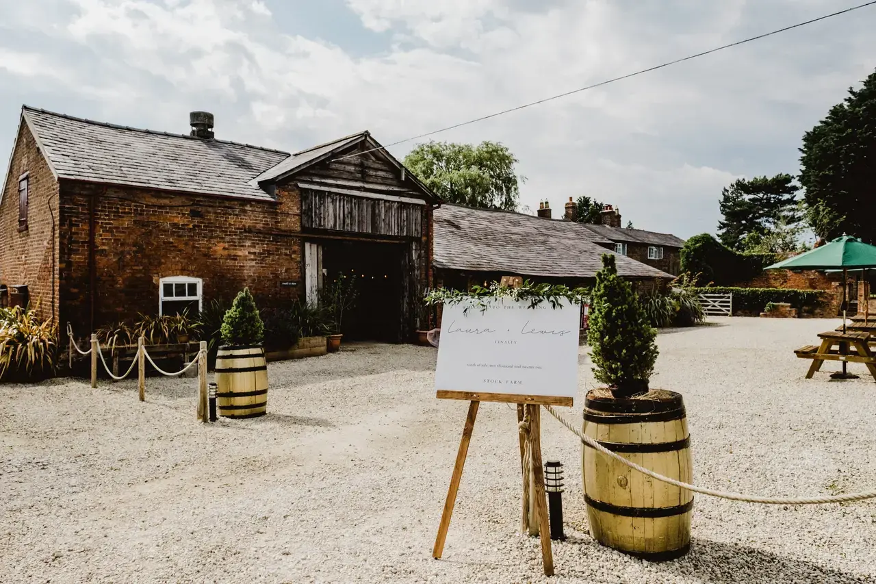 A wedding welcome sign on an easel outside of a brick barn wedding venue in Cheshire