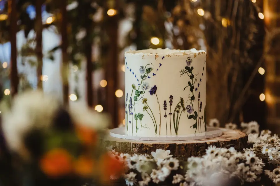 A hand-painted single tier white wedding cake with dainty flowers and foliage painted on the side