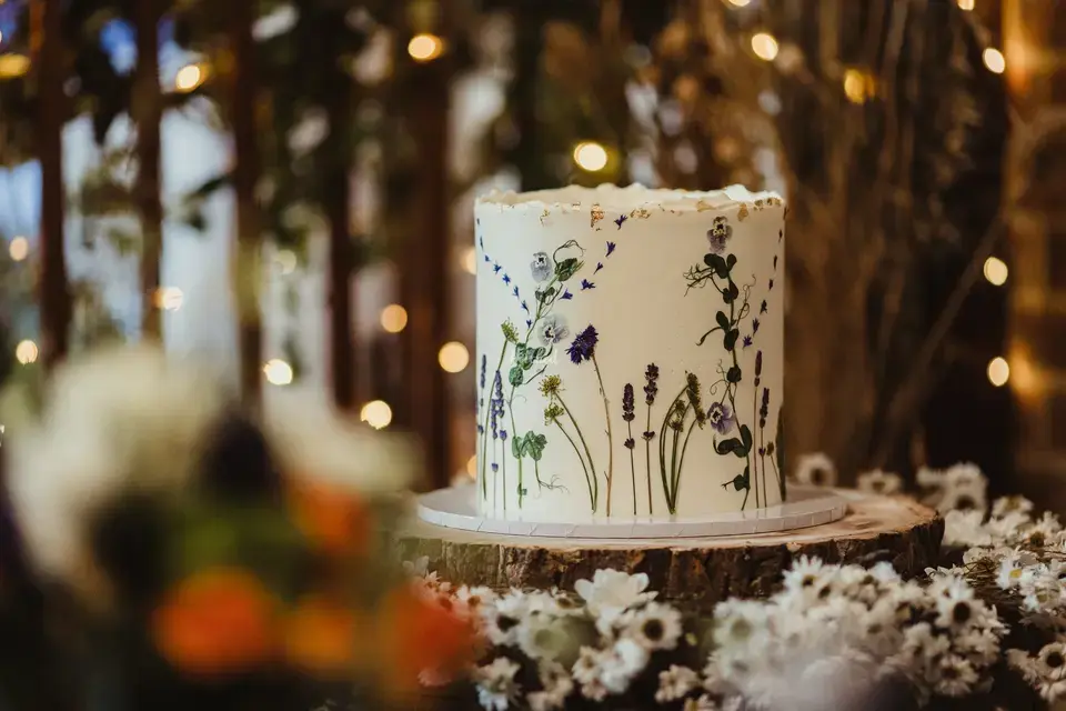 A hand-painted single tier white wedding cake with dainty flowers and foliage painted on the side