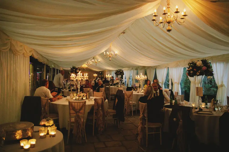 Marquee wedding venue space laid for a wedding reception with candles and floral arrangements as guests sit and chat