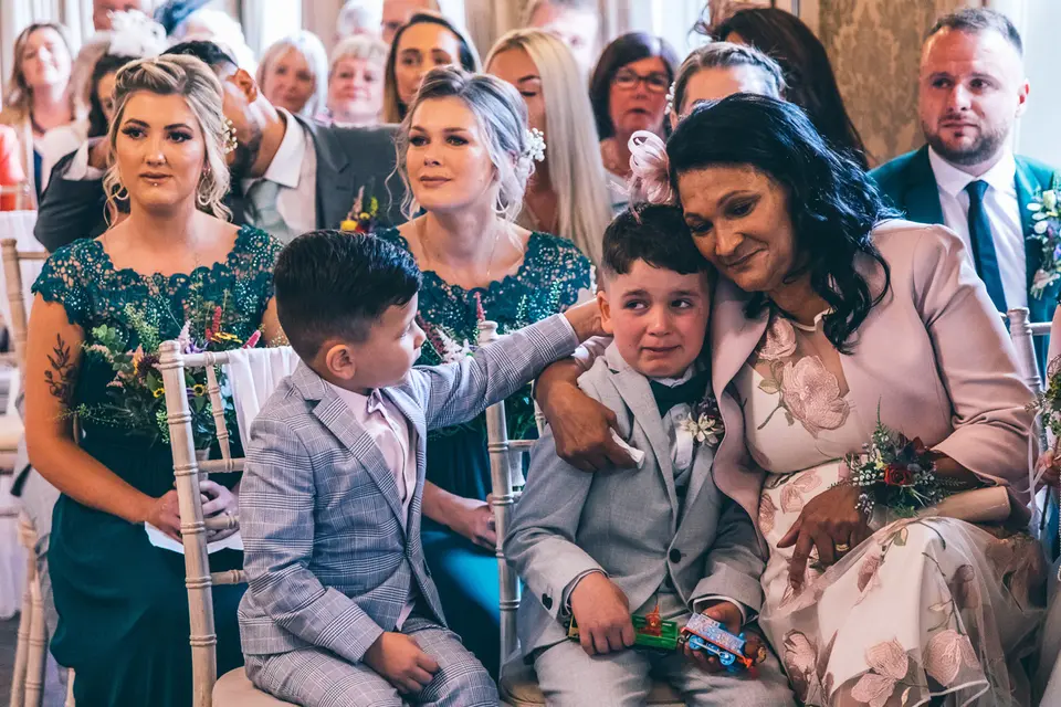 Mother of the bride comforting two emotional page boys as the guests watch the wedding ceremony